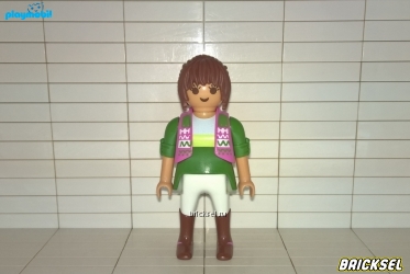 Женщина с короткими каштановыми волосами в оливково-зеленой кофте, зелено-розовой жилетке, белых брюках и коричневых сапогах
